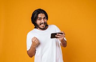 Indian man with mobile in hand looking happy over orange background