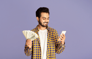 Indian guy looking at mobile smiling and holding cash in his other hand
